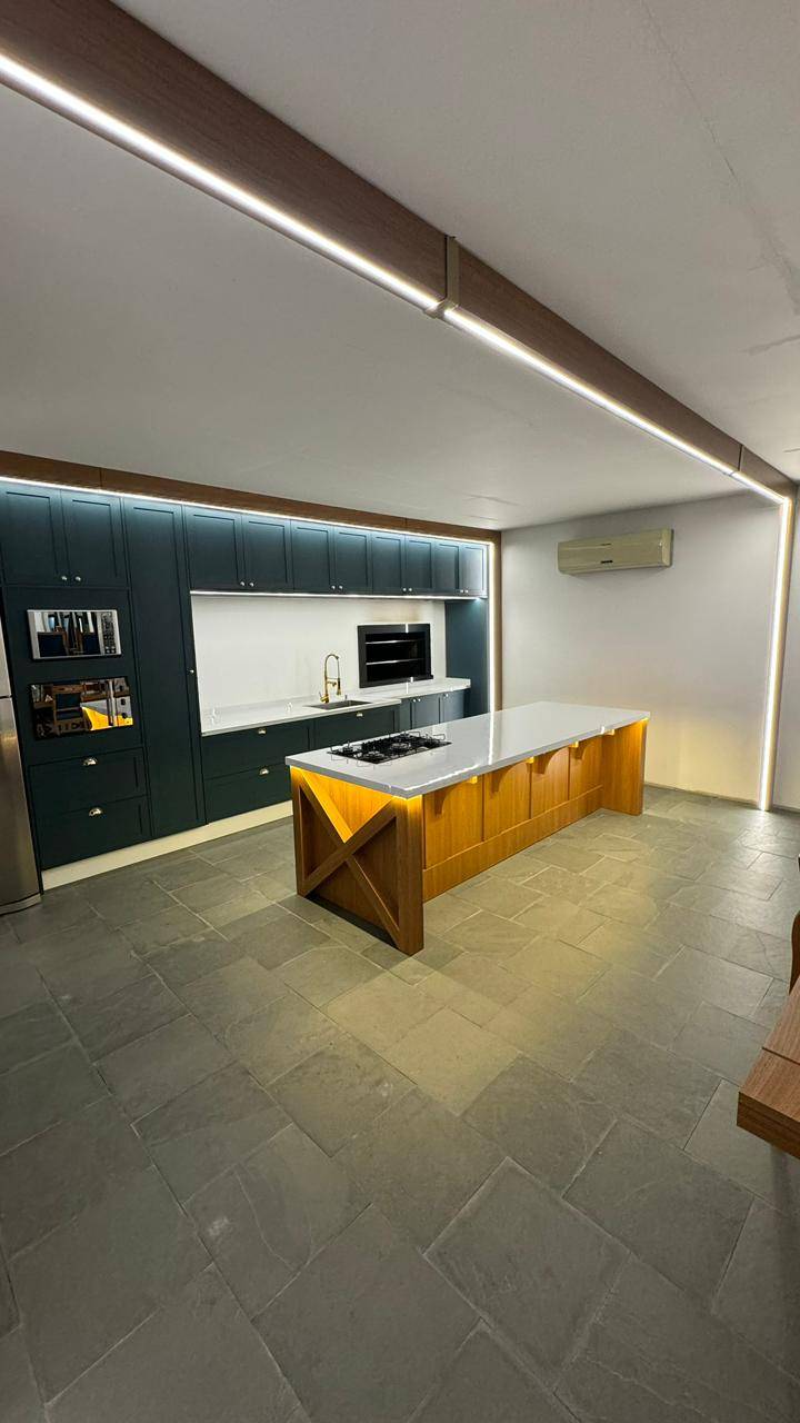 Cozinha com bancadas em porcelanato cinza, armários escuros e iluminação linear.